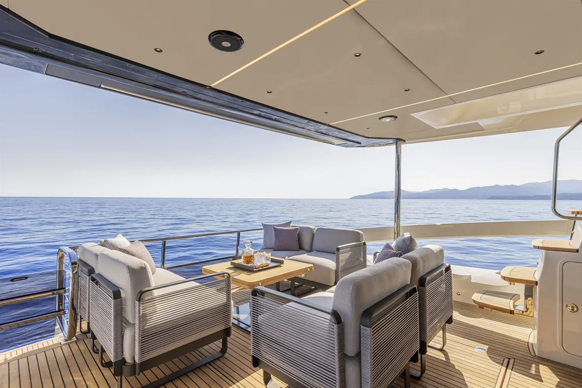 Luxurious yacht deck with stylish seating, coffee table, and ocean view, perfect for relaxation under a clear sky.